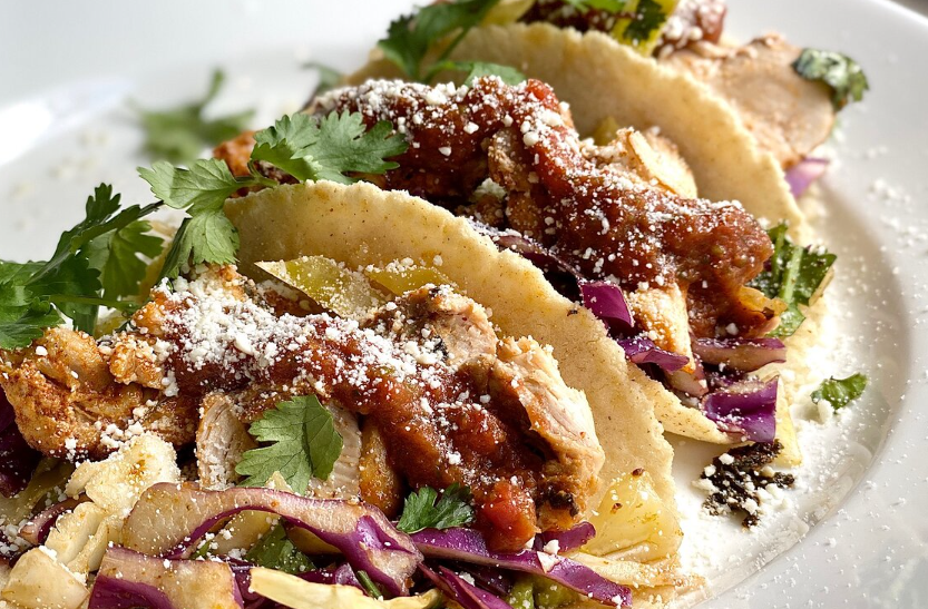 Three tacos packed with cultural flavors, adorned with slaw and cilantro.