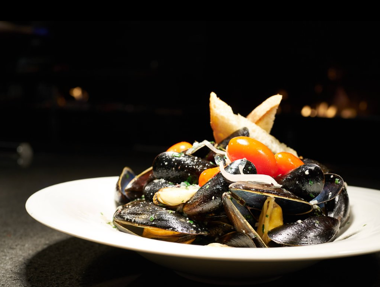 A platter of succulent mussels and fresh vegetables beautifully arranged on a rustic table, embodying the quintessential New England charm of Groton Massachusetts